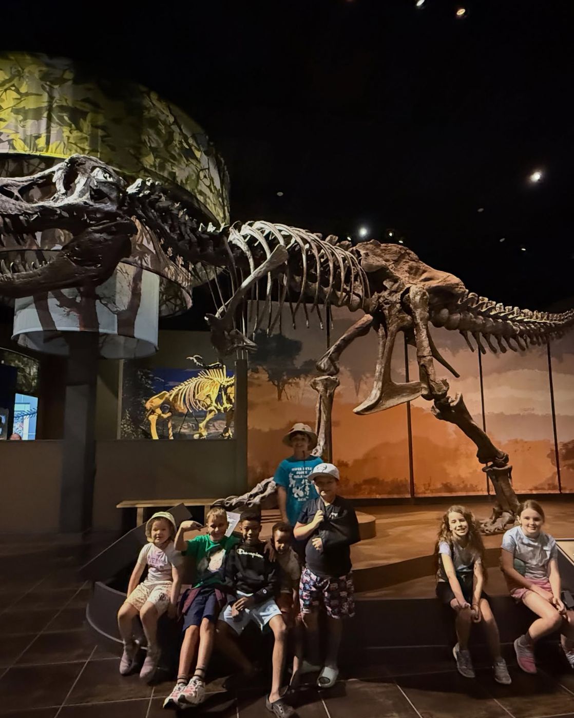 Campers posing under a T. rex skeleton at a natural history museum