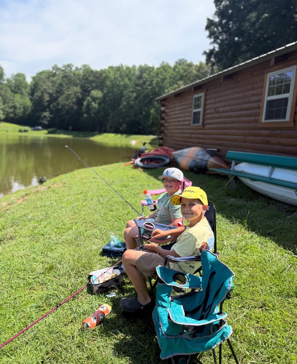 Two campers fishing at a pond by a log cabin
