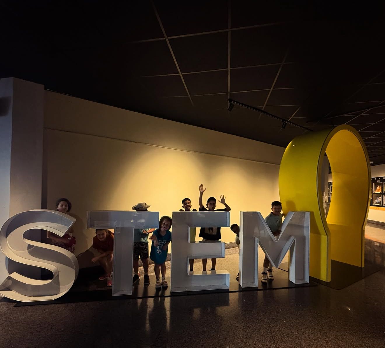 Campers waving from behind giant STEM letters at a science center