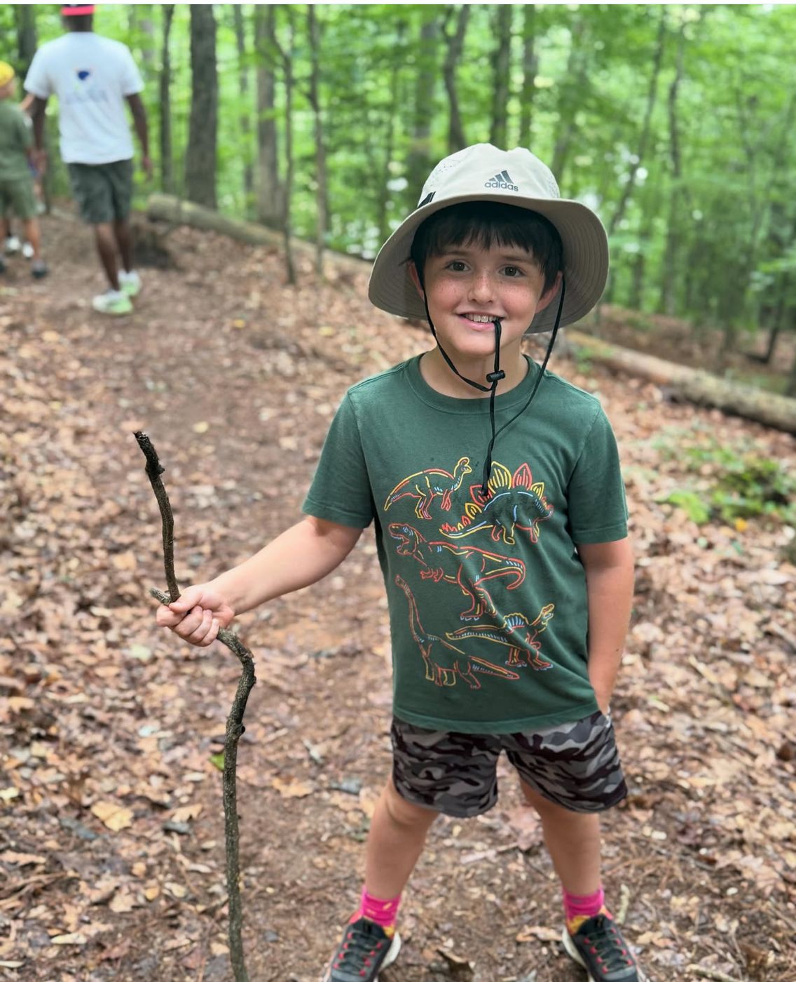 Smiling camper with a walking stick on a forest trail