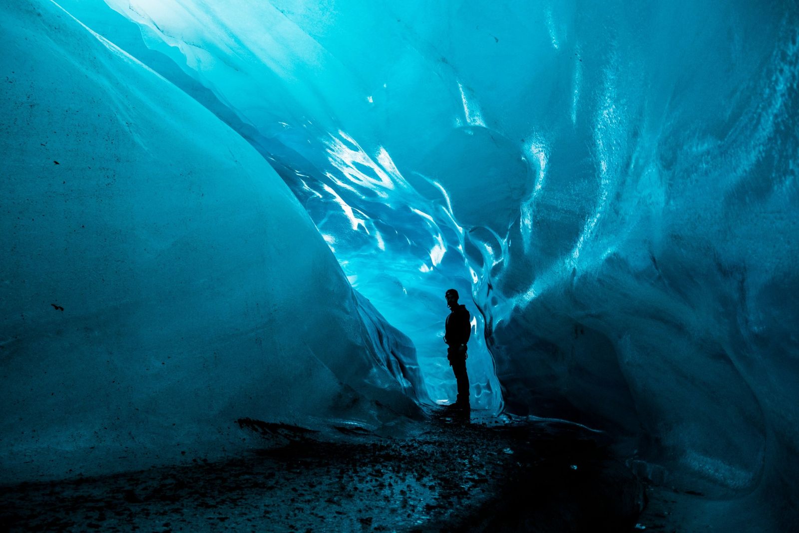 Person standing in a blue glacier ice tunnel